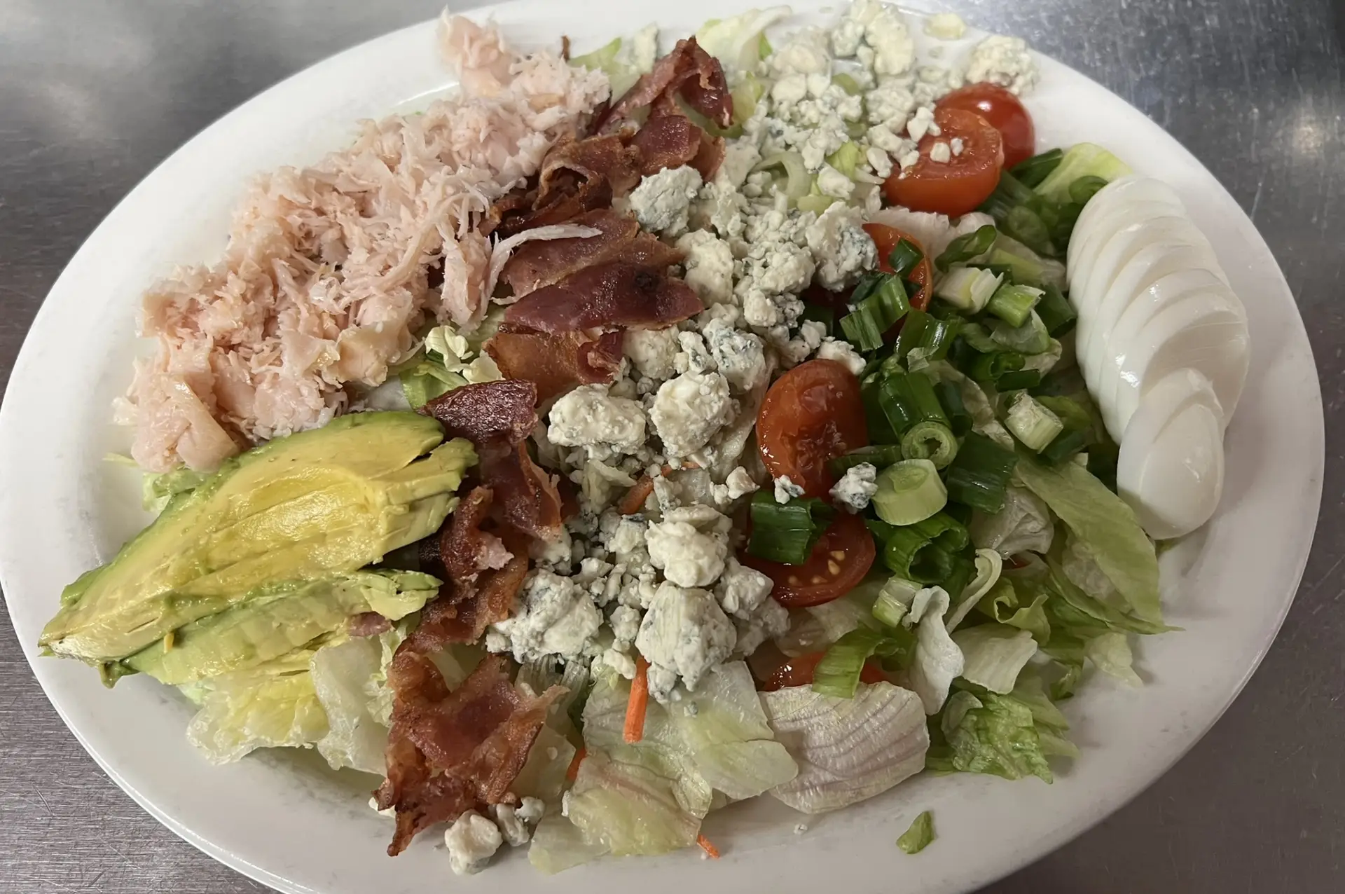 A fresh salad featuring crispy bacon, ripe tomatoes, avocado, crisp lettuce, and shredded cheese, arranged in a vibrant plate